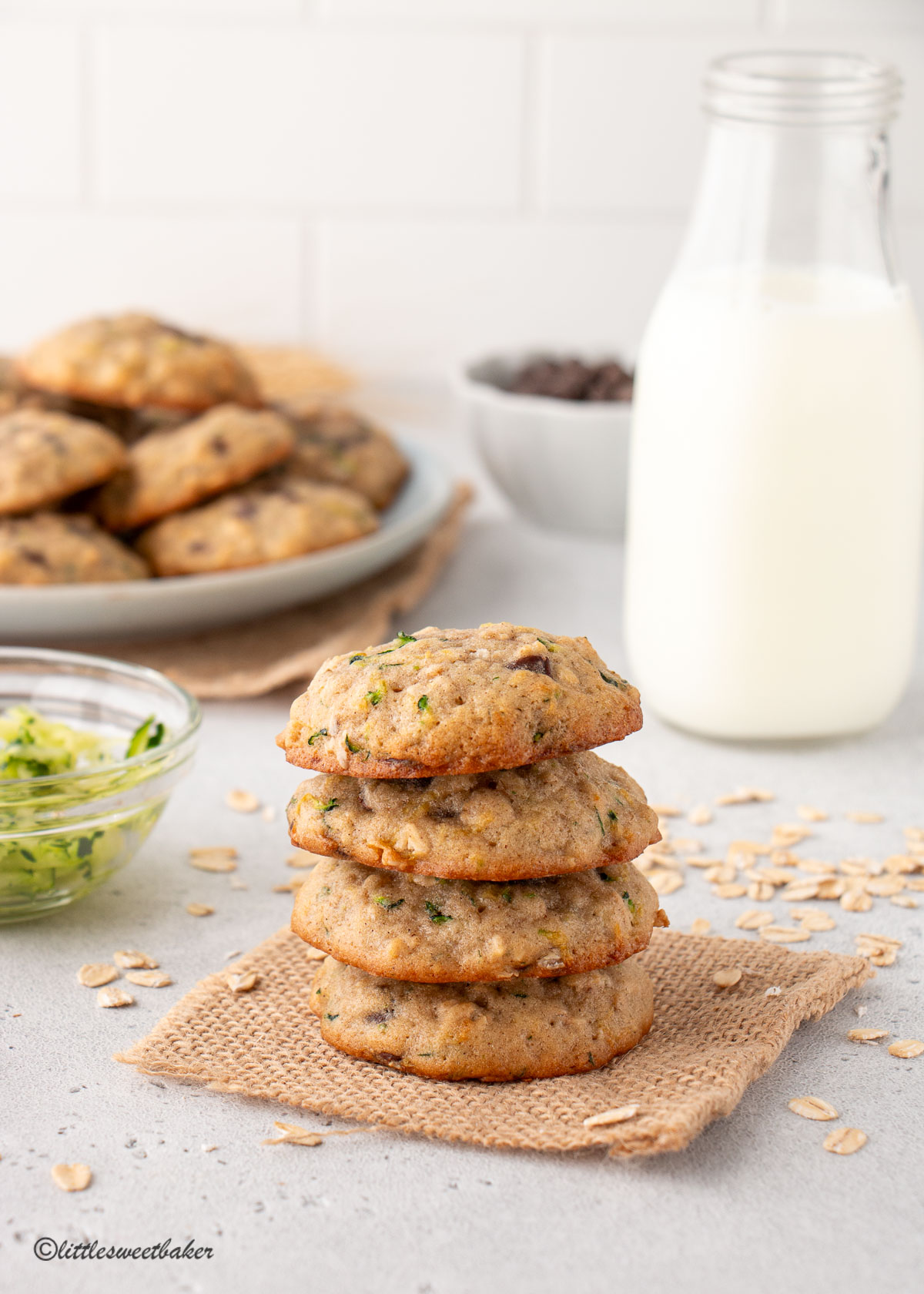 A stack of zucchini oatmeal cookies with a glass of milk and plate of cookies in the background.