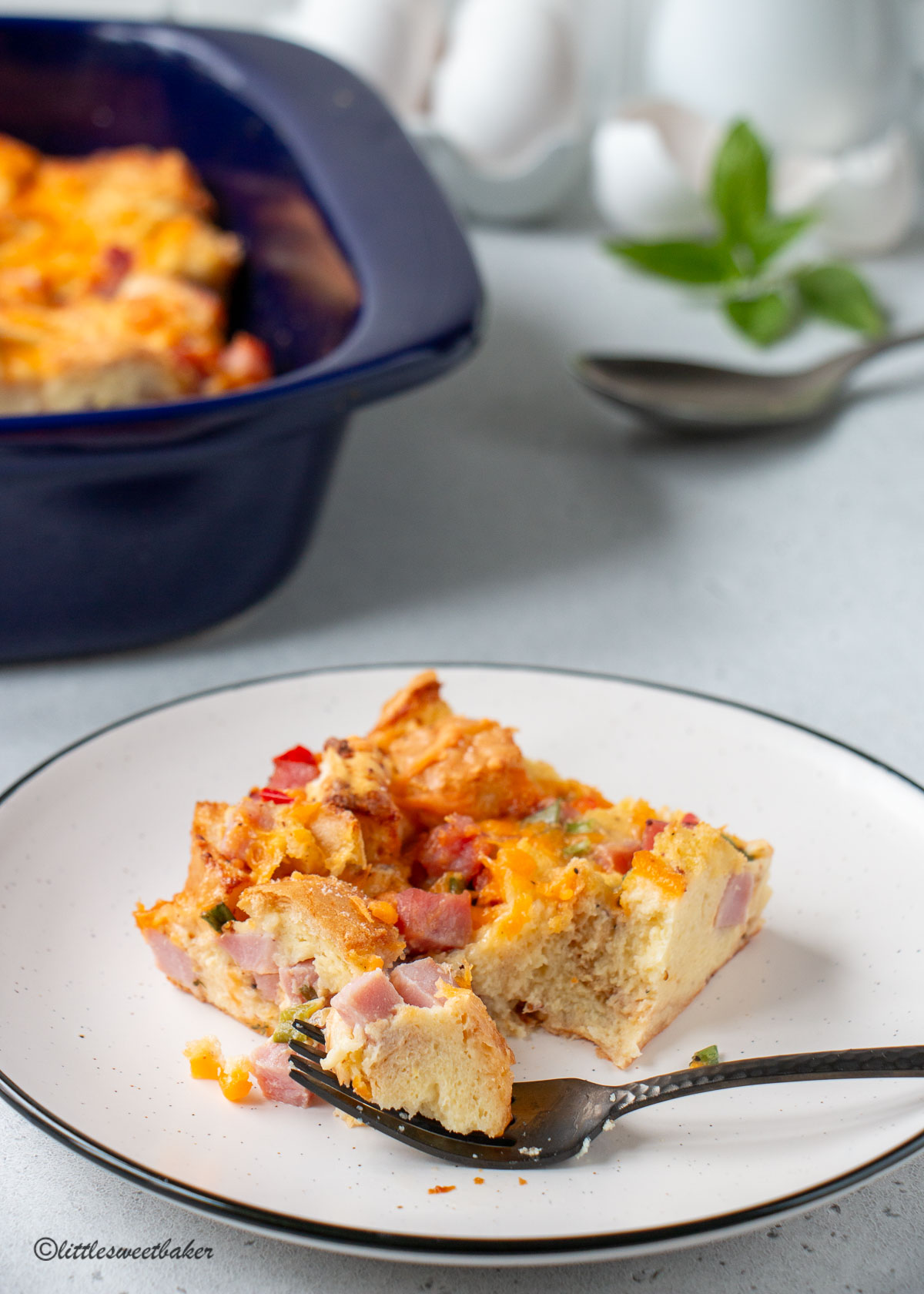 A slice of breakfast casserole on a plate with a piece on a fork.