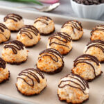Chocolate drizzled coconut macaroons lined up on a baking sheet.