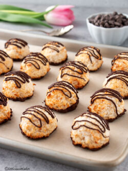 Chocolate drizzled coconut macaroons lined up on a baking sheet.