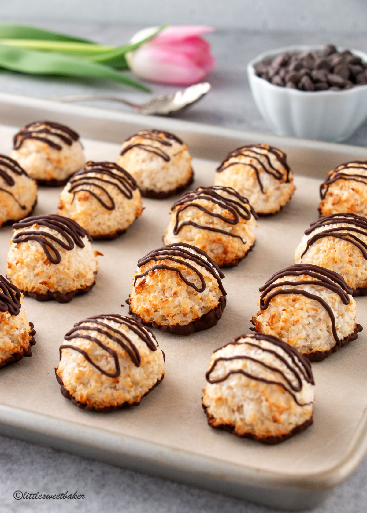 Chocolate drizzled coconut macaroons lined up on a baking sheet.
