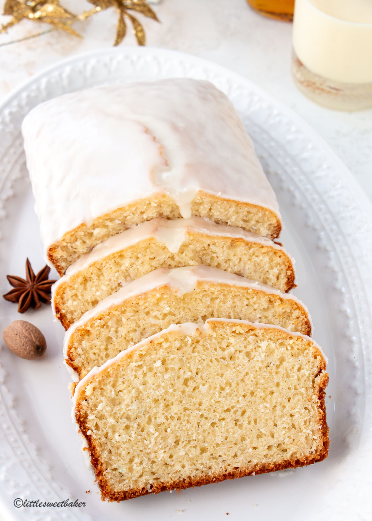 A loaf of glazed eggnog bread on a serving plate with a few cut slices.