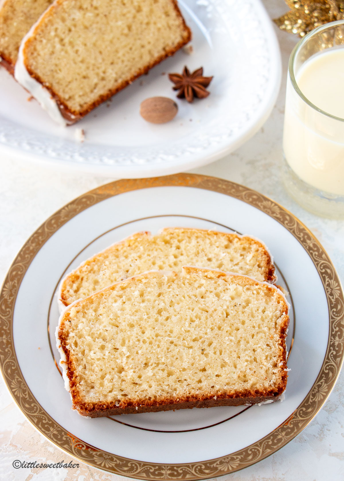 Two slices of eggnog bread with rum glaze on a white and gold plate