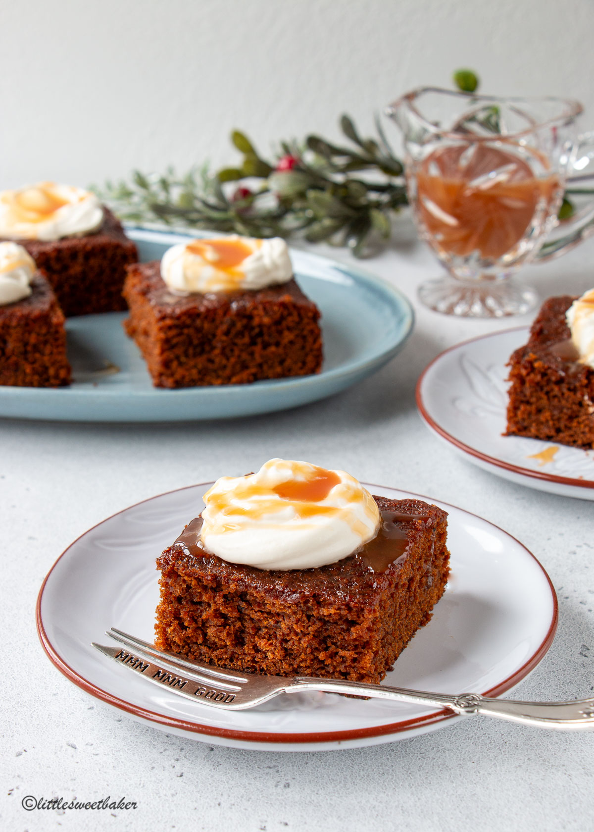 A slice of gingerbread cake topped with whipped cream and caramel on a grey plate.