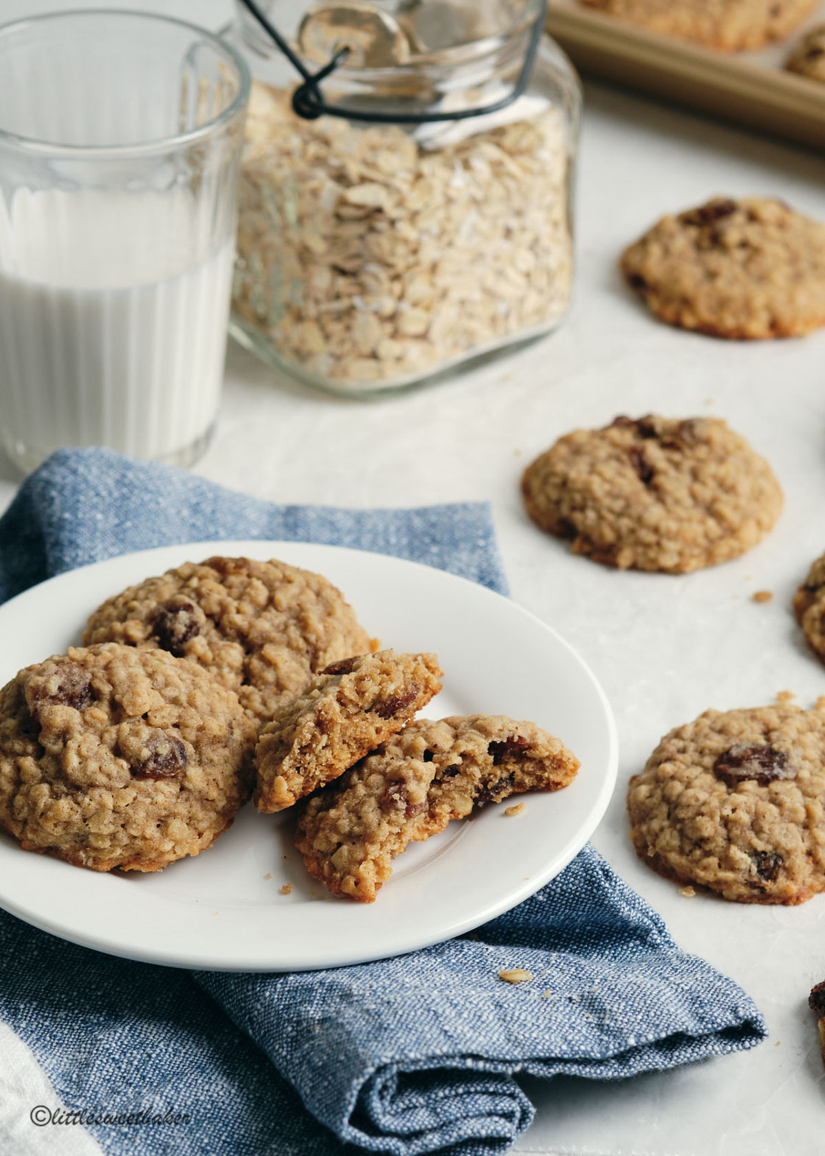 Oatmeal raisin cookies on a plate and denim napkin with one cookie broken in half.