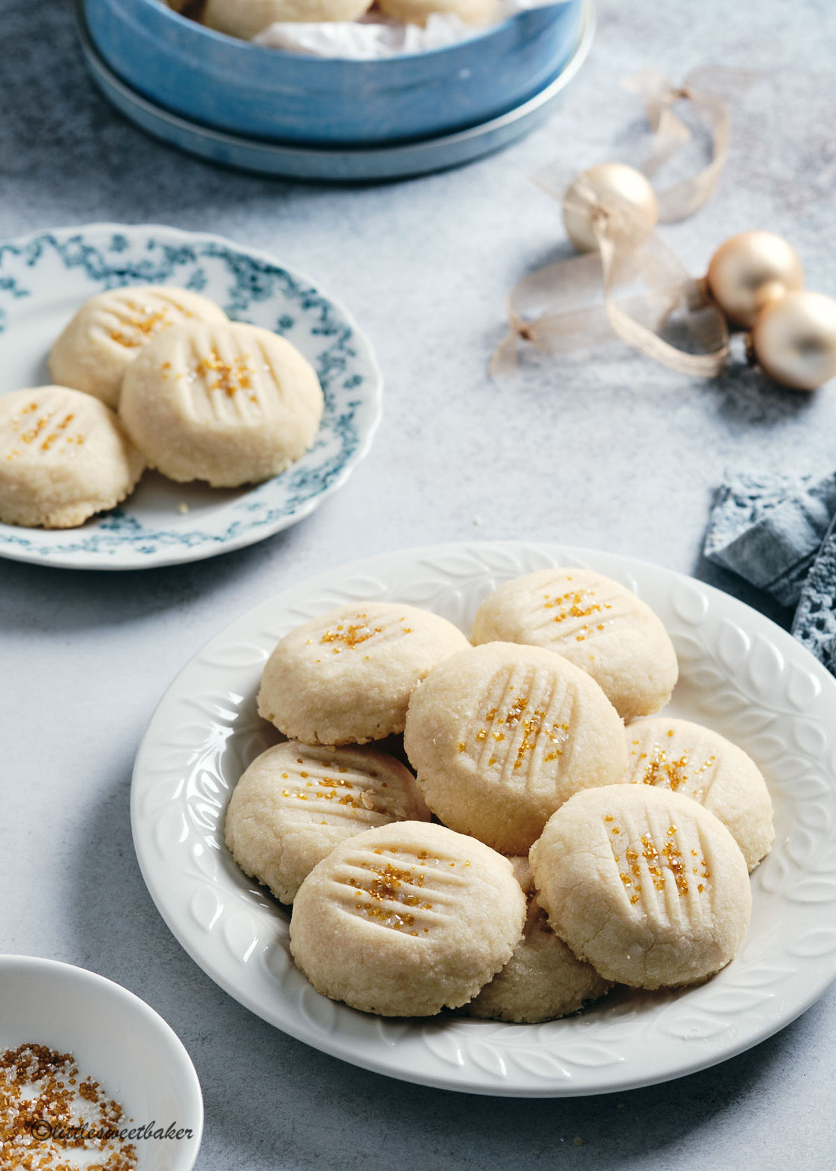 A plate of whipped shortbread cookies with gold sprinkles.