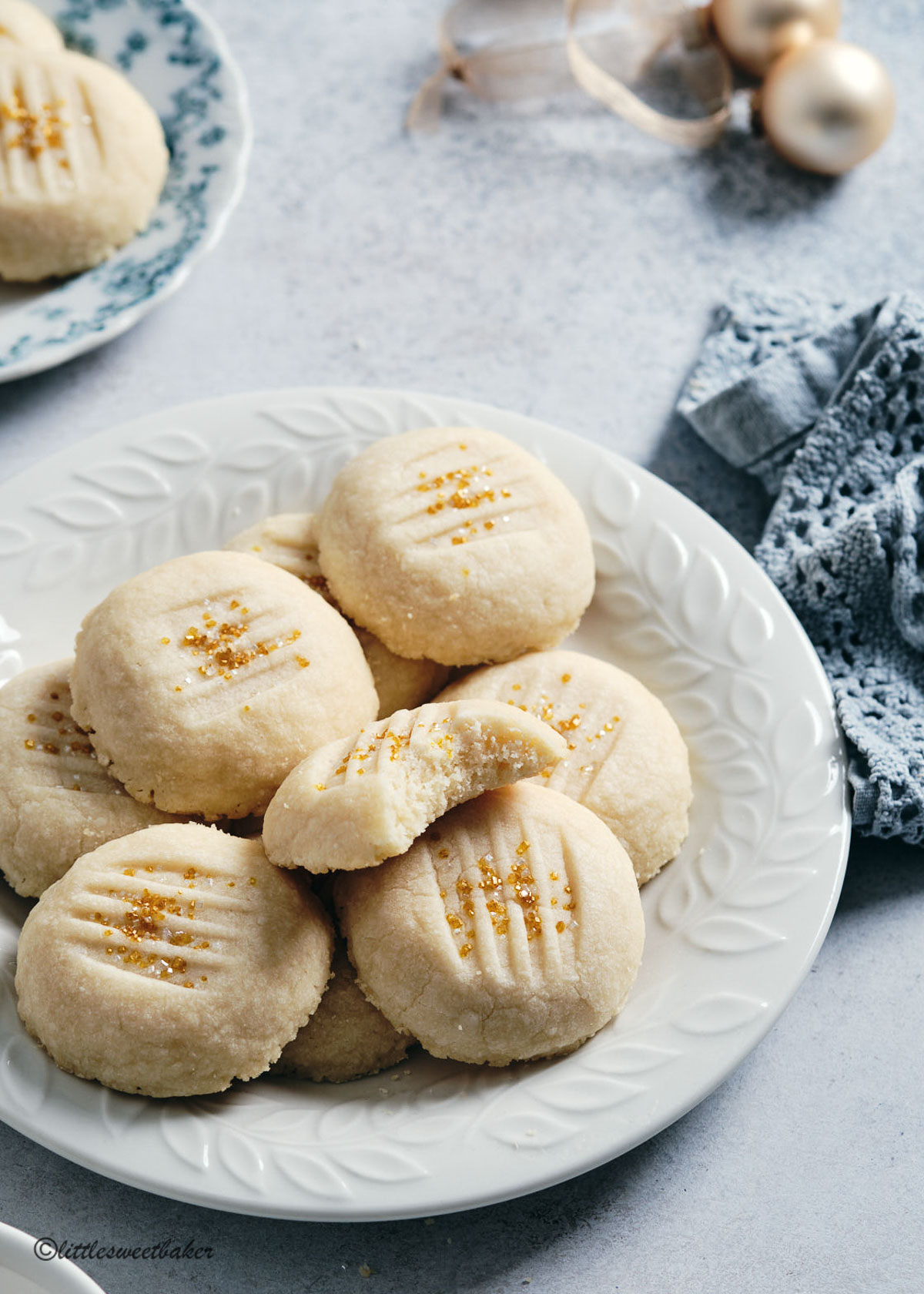 Whipped shortbread cookies on a white plate with a bite taken out of one of the cookies.