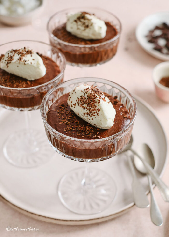 3 glasses of chocolate mousse topped with whipped cream on a serving plate