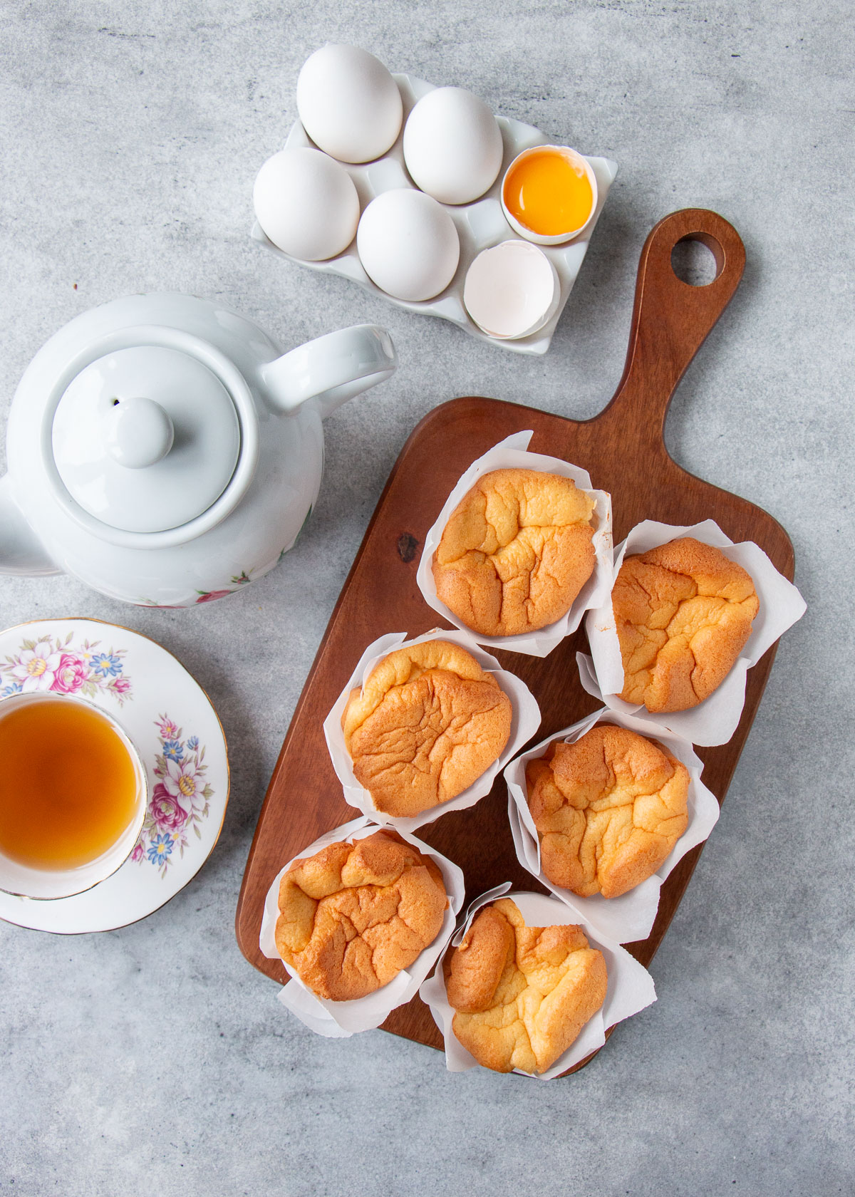 Overhead view of paper-wrapped sponge cakes on a wooden board with teapot and teacup.