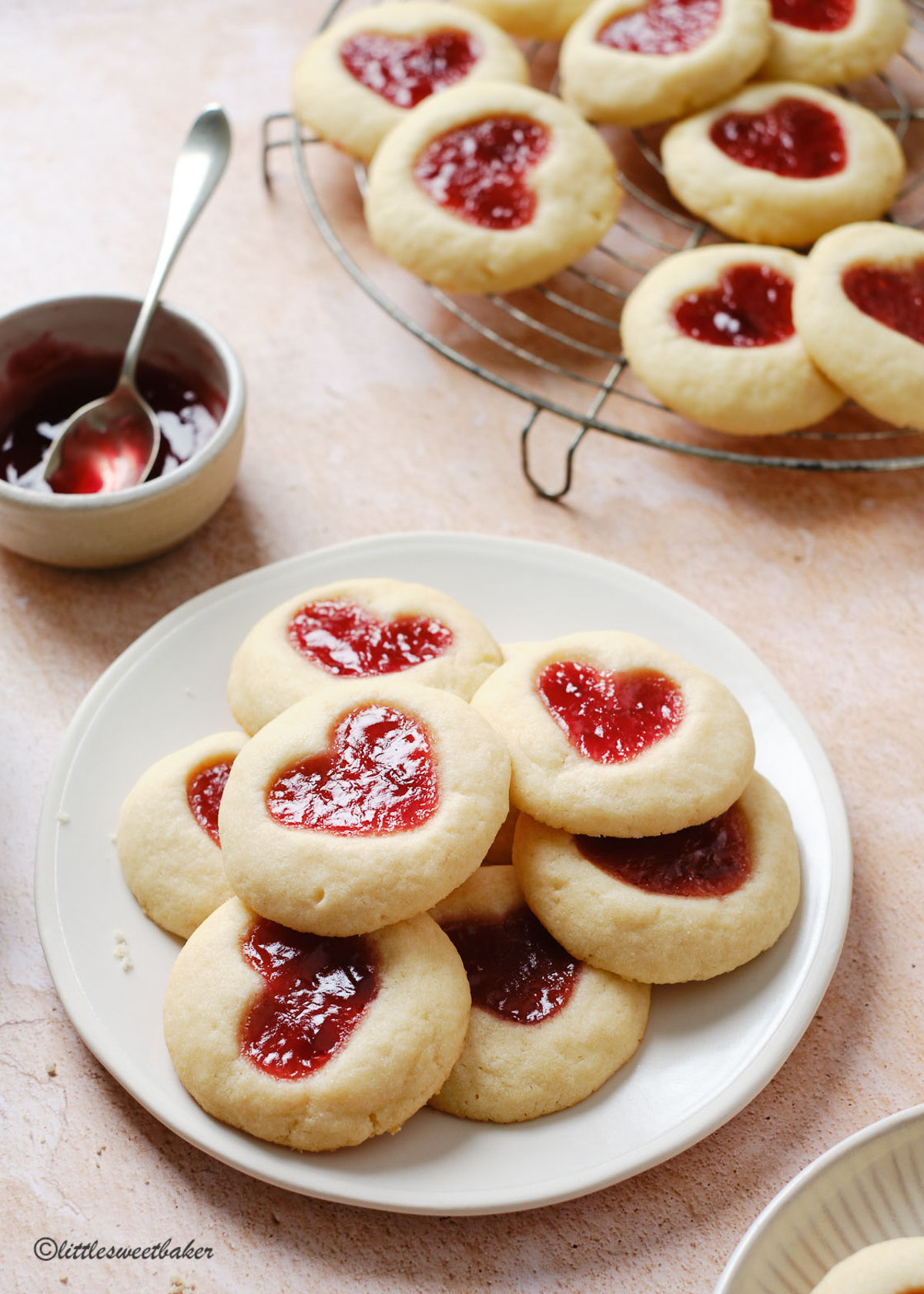 Heart-shaped strawberry thumbprint cookies on a plate and some on a cooling rack