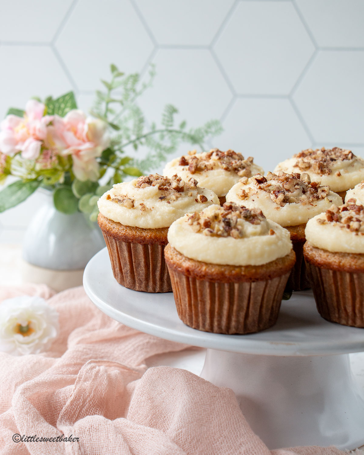 carrot cake cupcakes on a cake stand with a pink napkin and flowers