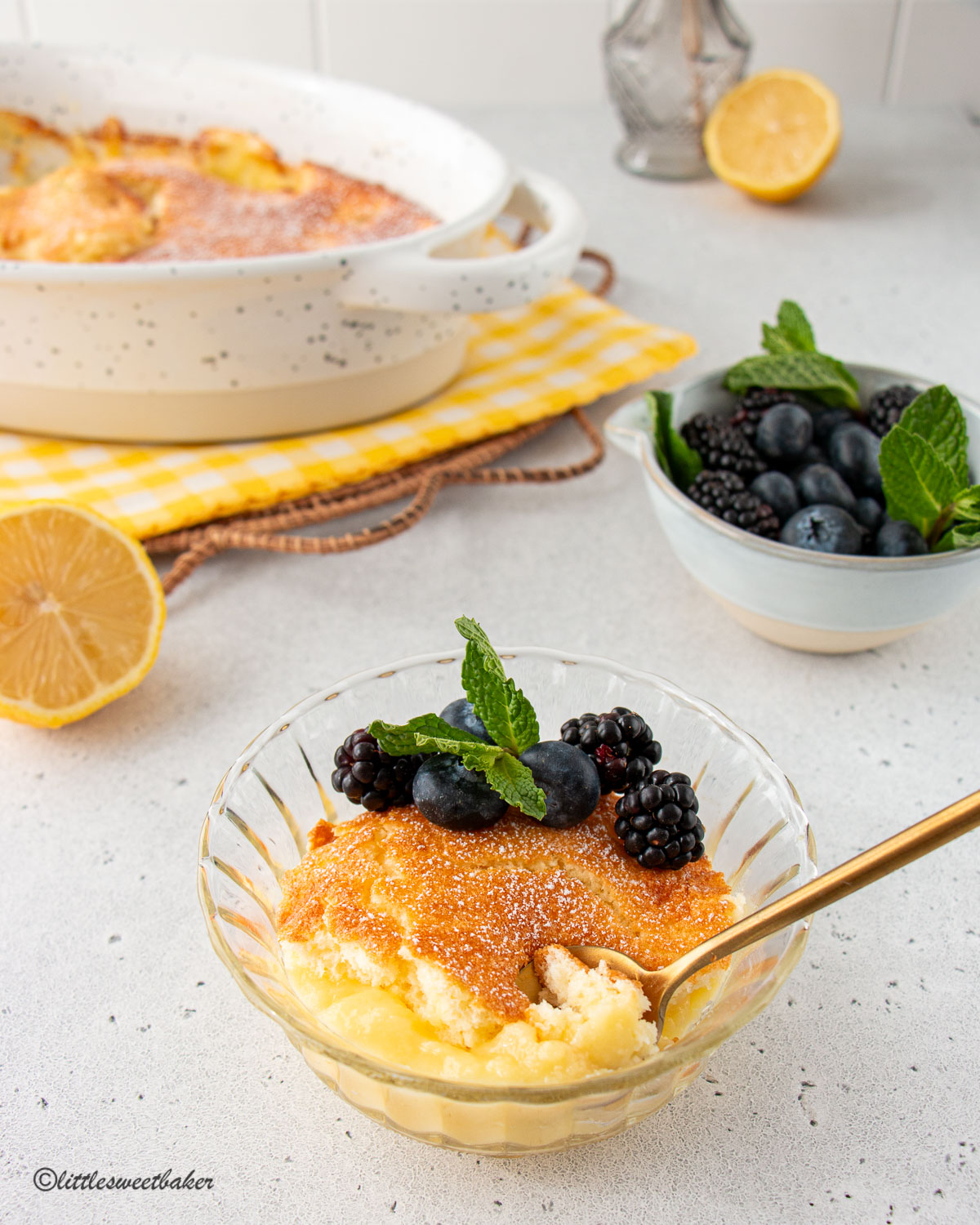 A bowl of lemon pudding cake with some berries and a sprig of mint.