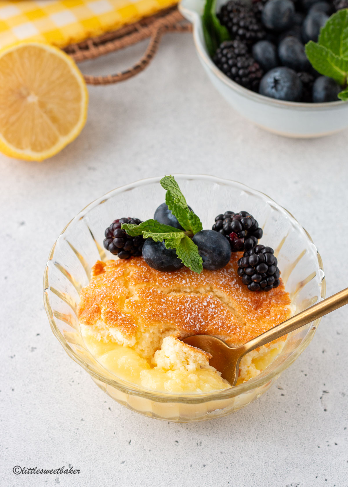 A bowl of lemon pudding cake with berries and gold spoon.