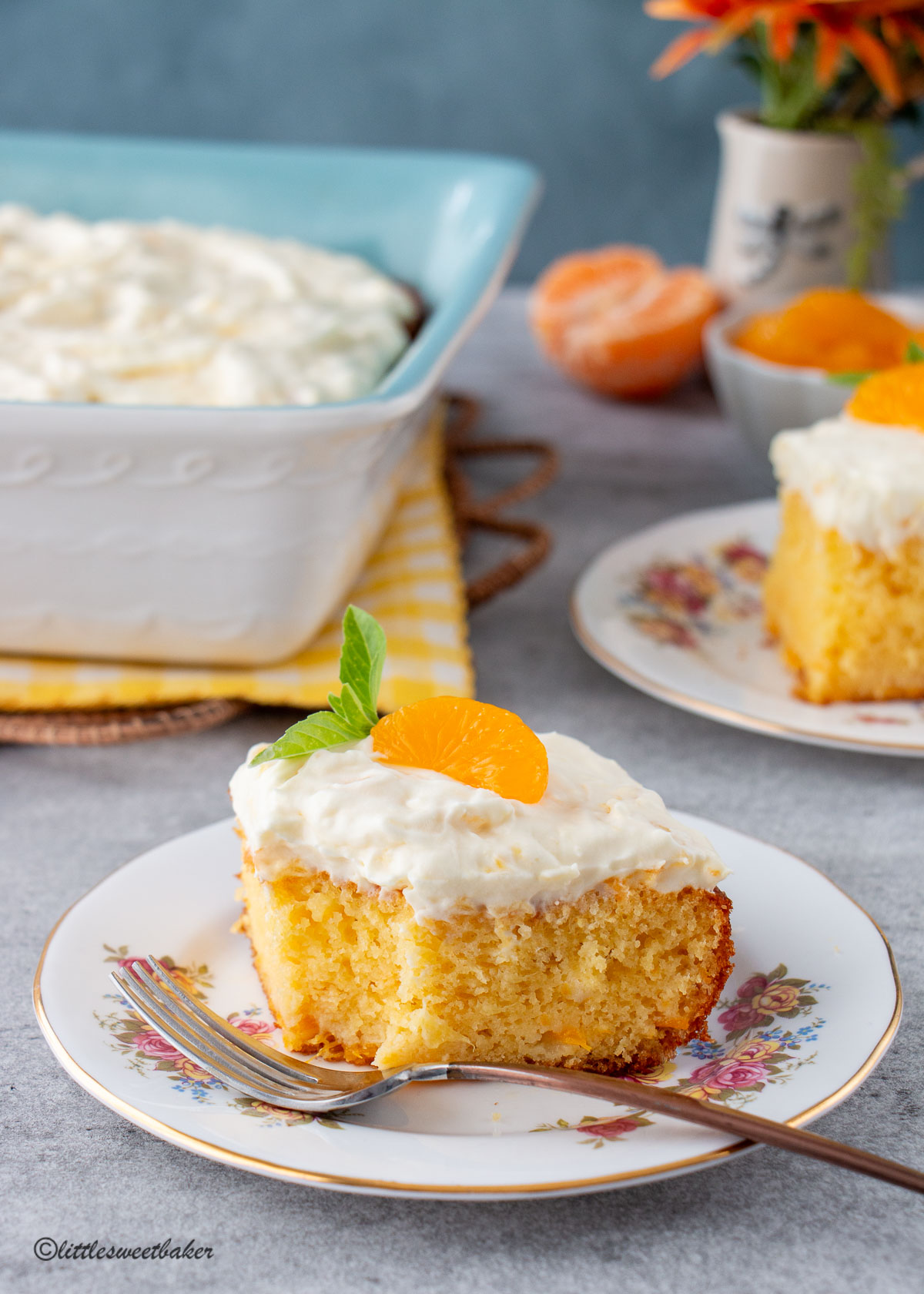 A slice of mandarin orange cake on a plate with a piece missing.