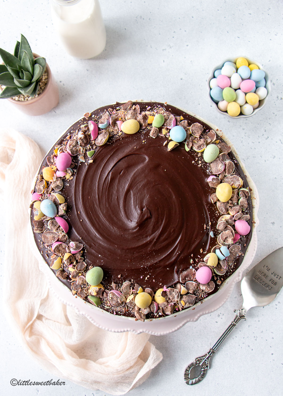 an overhead view of a mini egg cheesecake topped with chocolate ganache with a light pink linen napkin and cake server