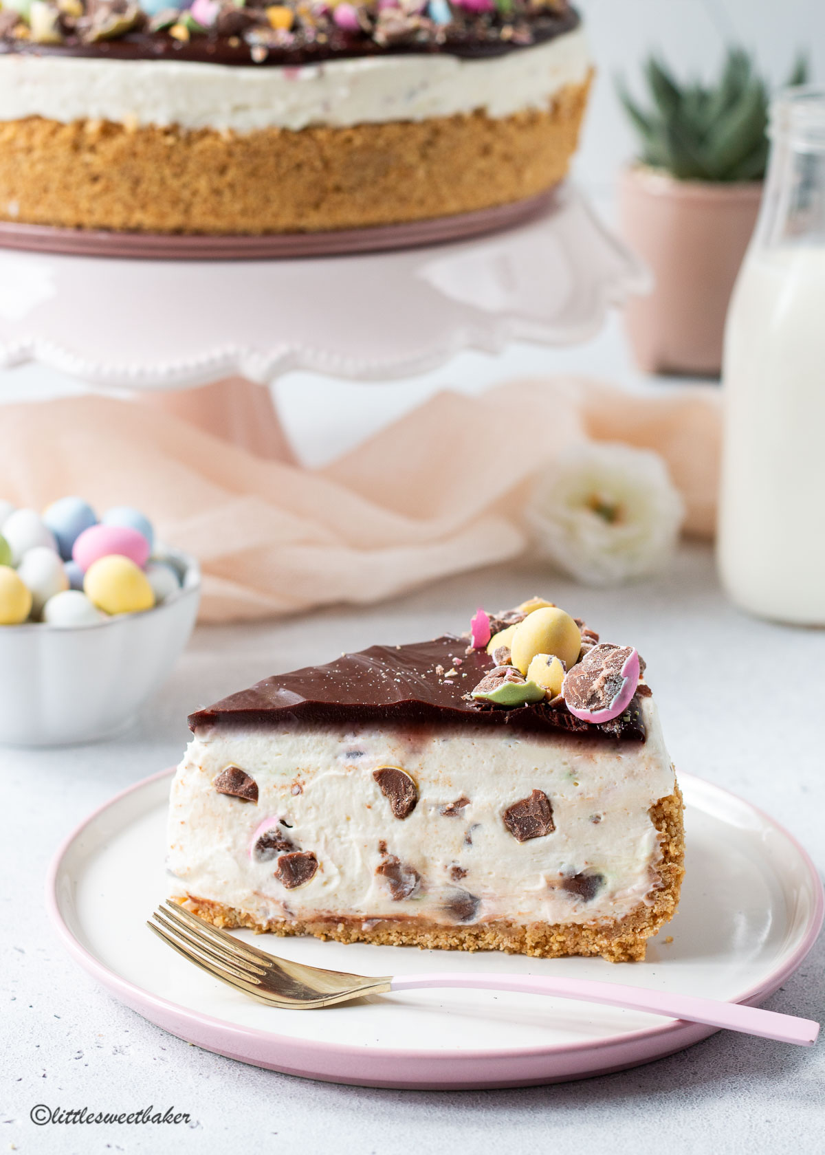 A slice of no-bake mini egg cheesecake on a pink and white plate with a pink and gold fork