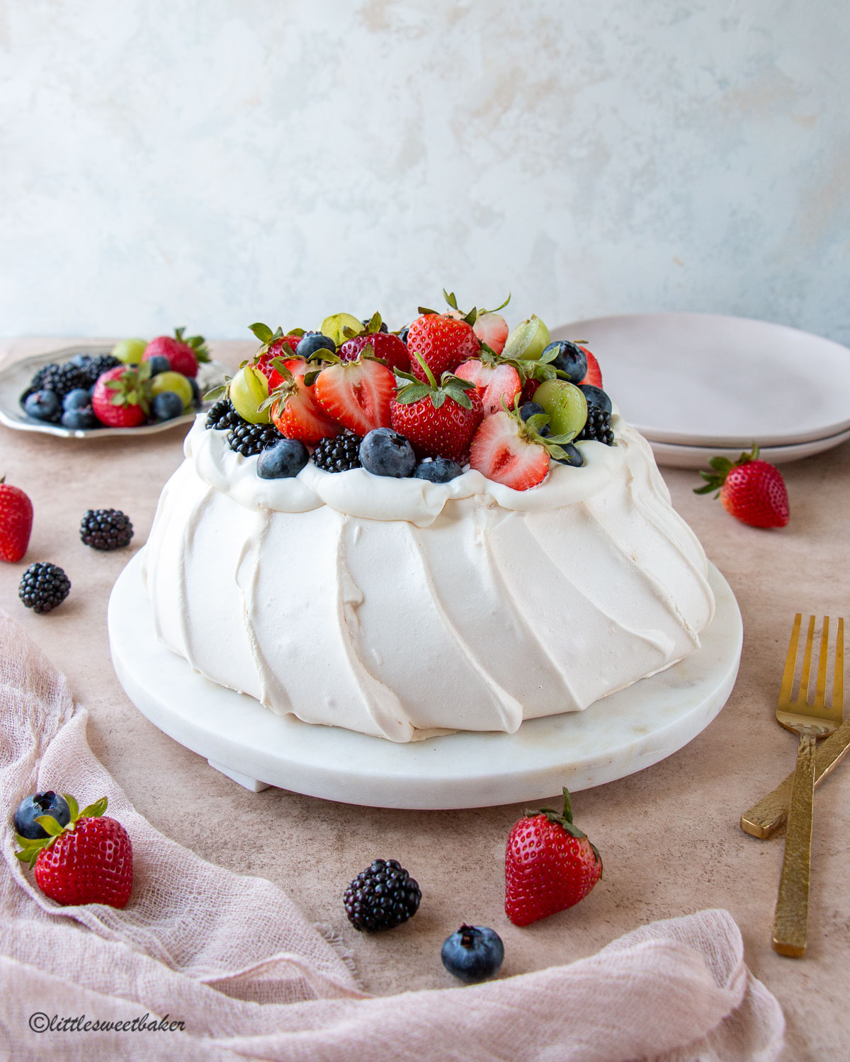 An easy pavlova topped with whipped cream and fruits on a marble serving plate.