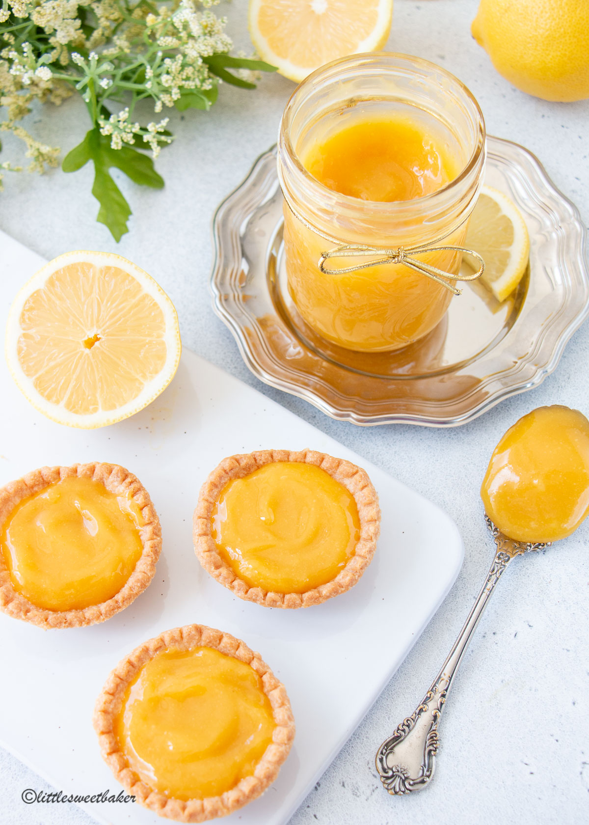 Lemon curd tarts on a white board with the jar and spoonful beside it.