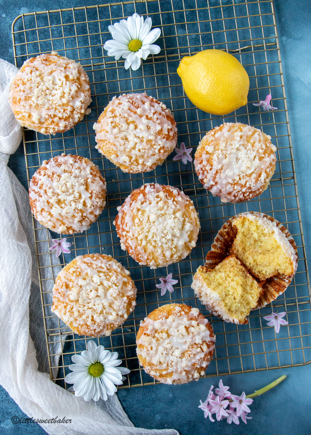 Lemon crumb muffins on a gold cooling rack with one muffin broken in half.