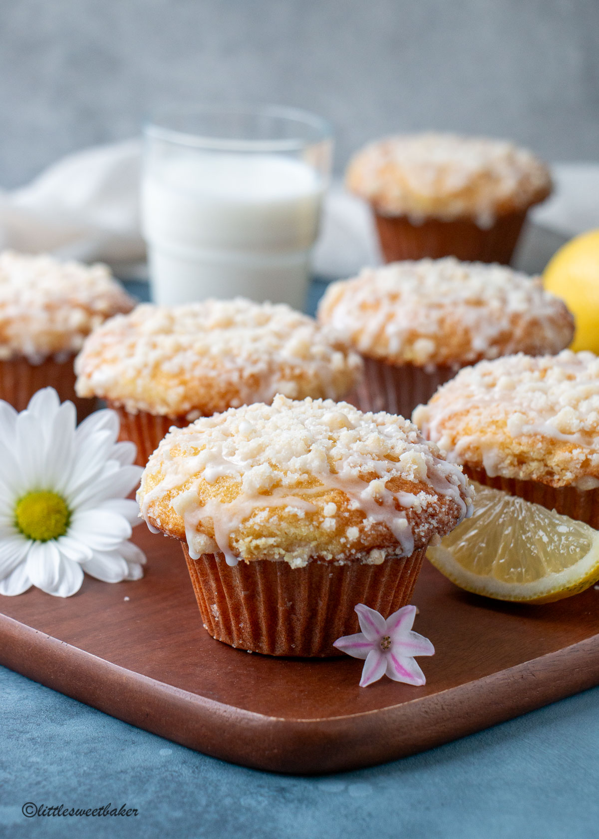 A bakery-style lemon muffins with crumb topping and glaze on a wooden board.