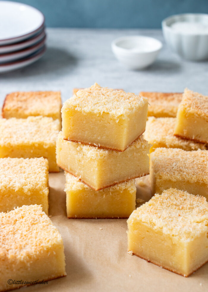 butter mochi cake squares scattered on parchment paper with 3 squares stacked in the middle