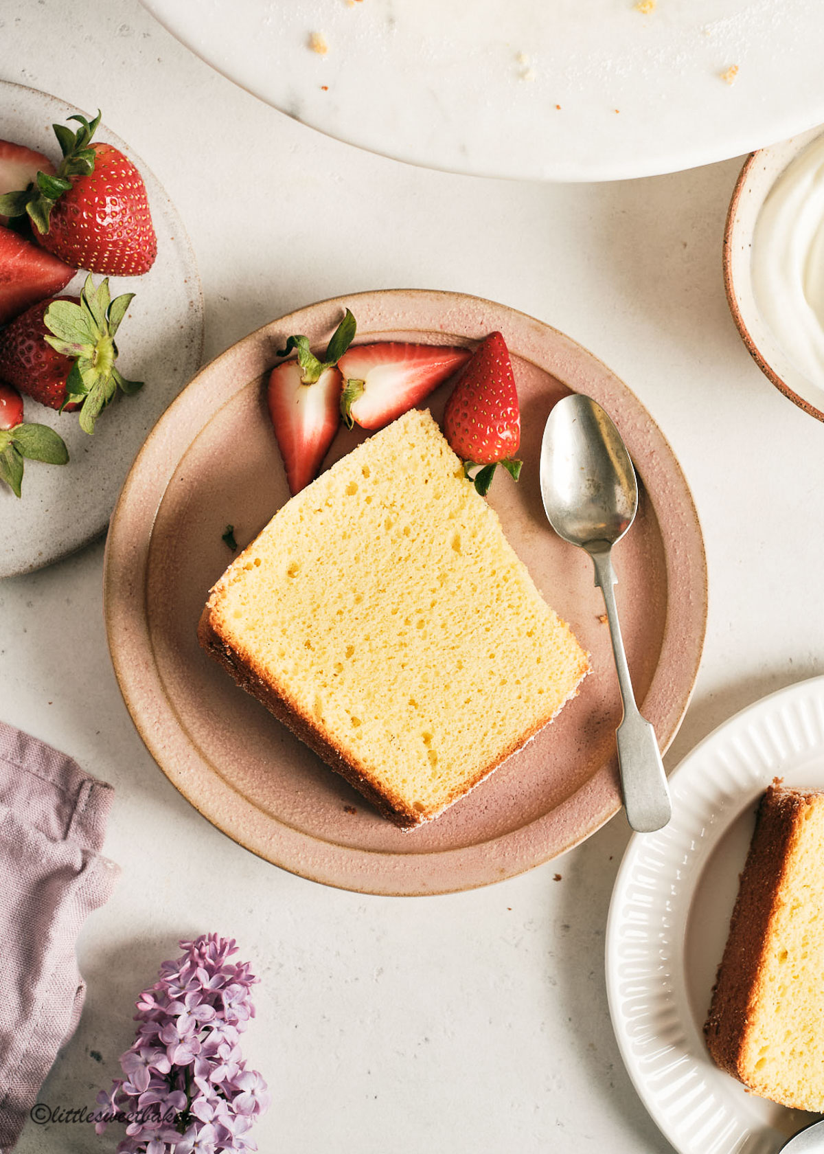 A slice of chiffon cake on a pink plate with strawberries and a spoon.