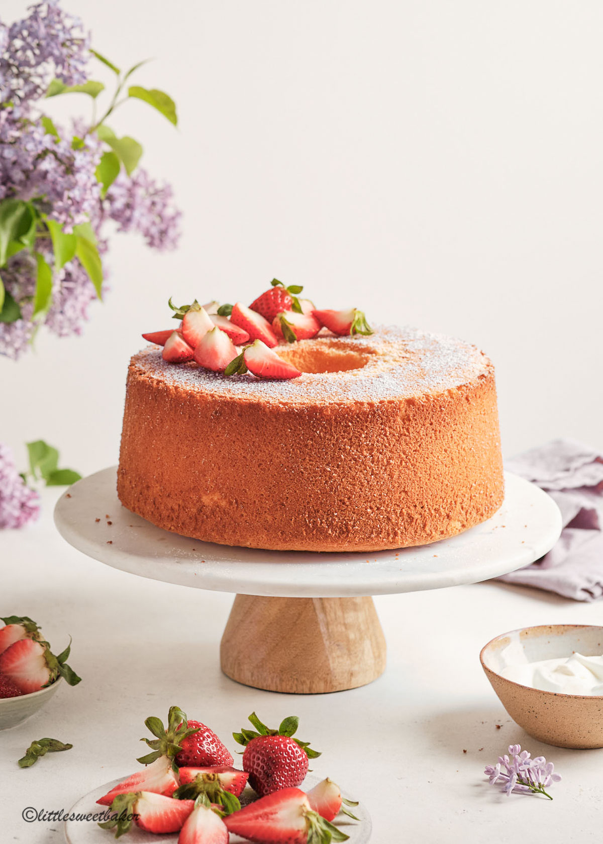 A vanilla chiffon cake topped with strawberries on a marble cake stand.