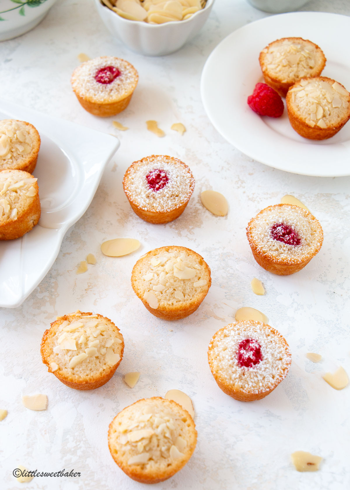 Mini financiers on a light speckled surface with almonds scattered around.