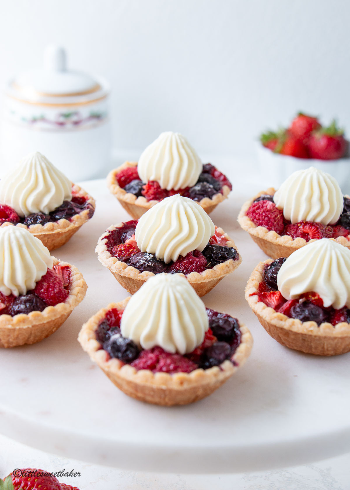 Mini berry pies topped with whipped cream on a marble cake stand.