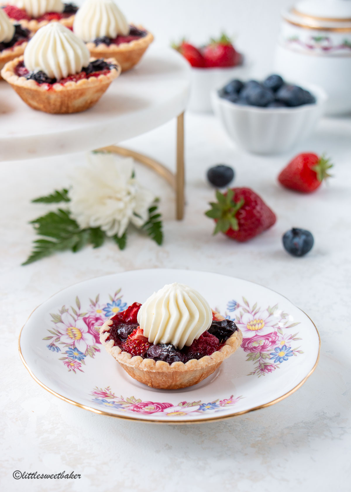 A mini berry tart on a vintage floral teacup saucer.