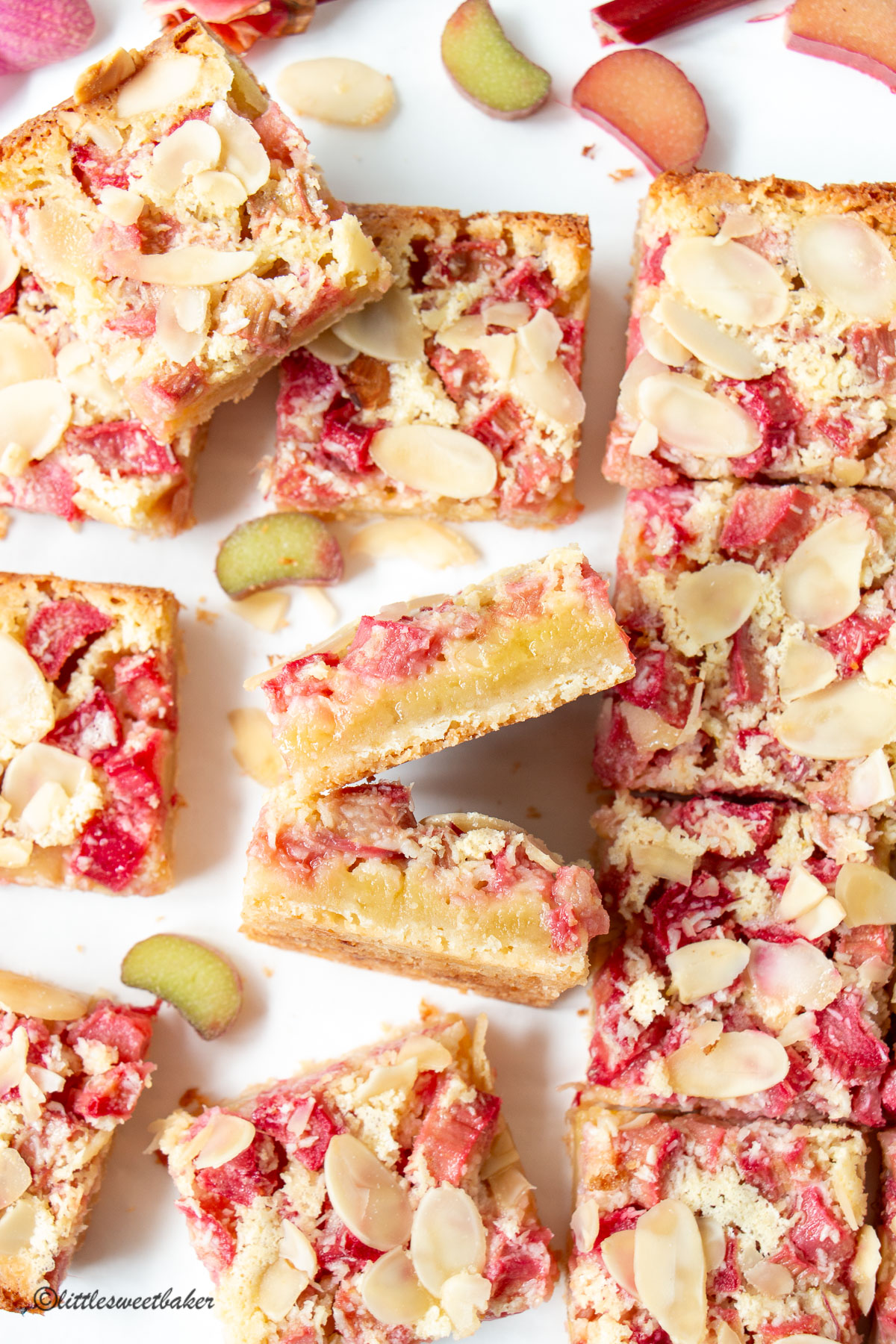 Rhubarb bars topped with almond slices scattered on a white surface.
