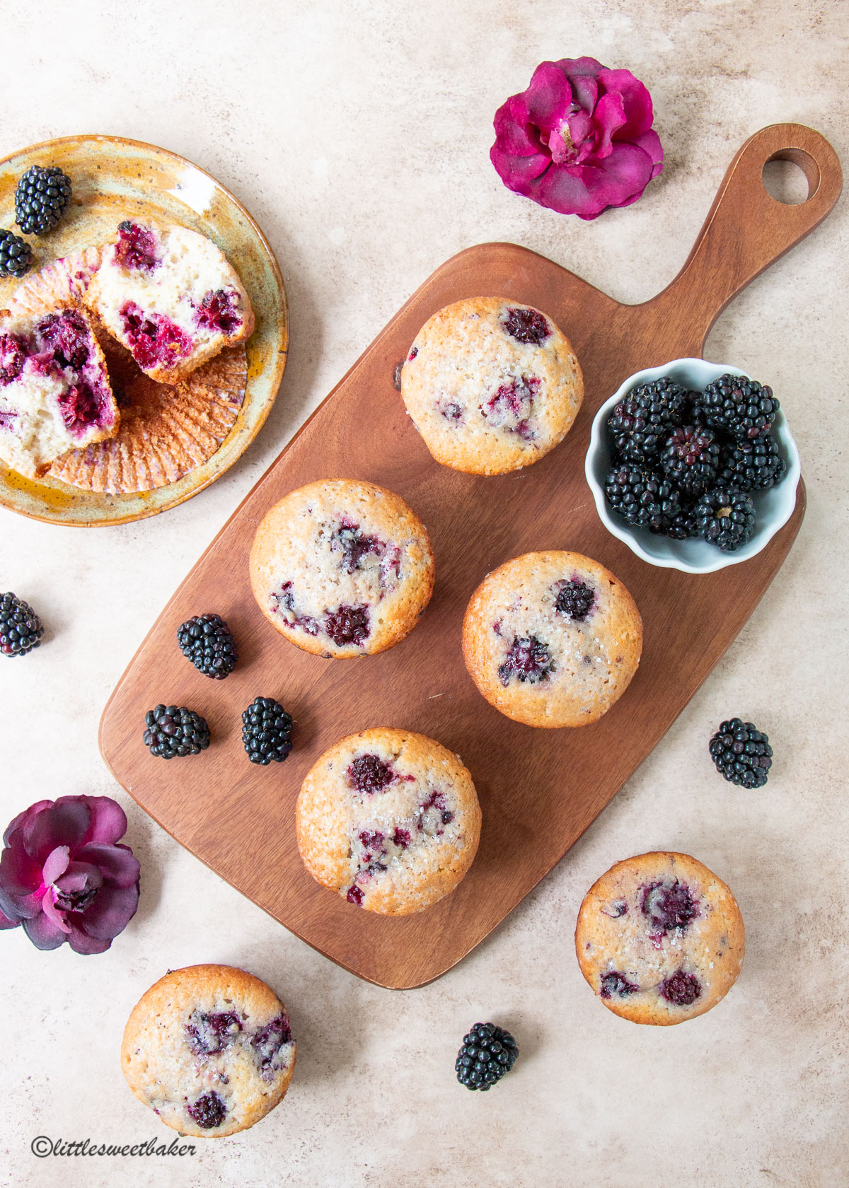 blackberry muffins on a wooden board with a bowl of blackberries and a muffin broken in half