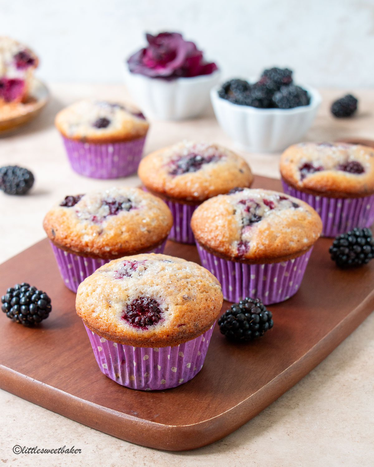 Blackberry muffins on a wooden board with blackberries scattered.