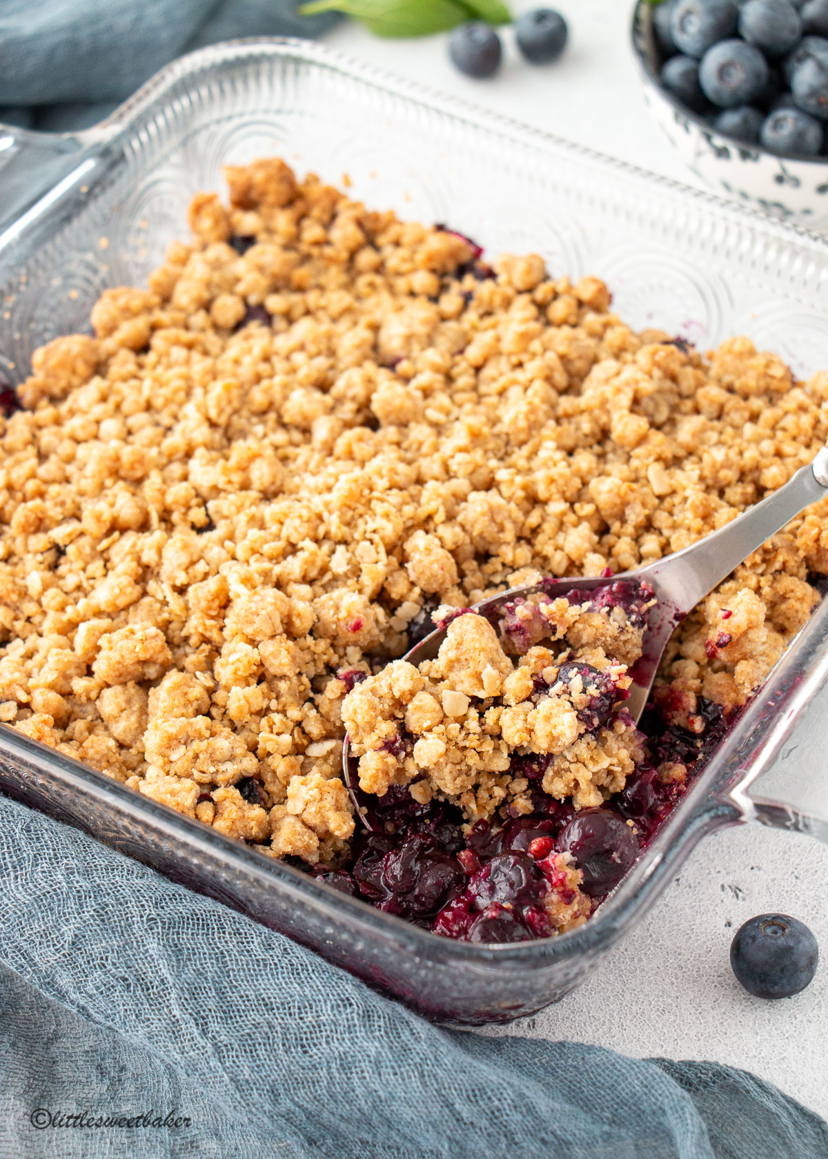 Blueberry crisp in a square glass dish with a serving spoon.