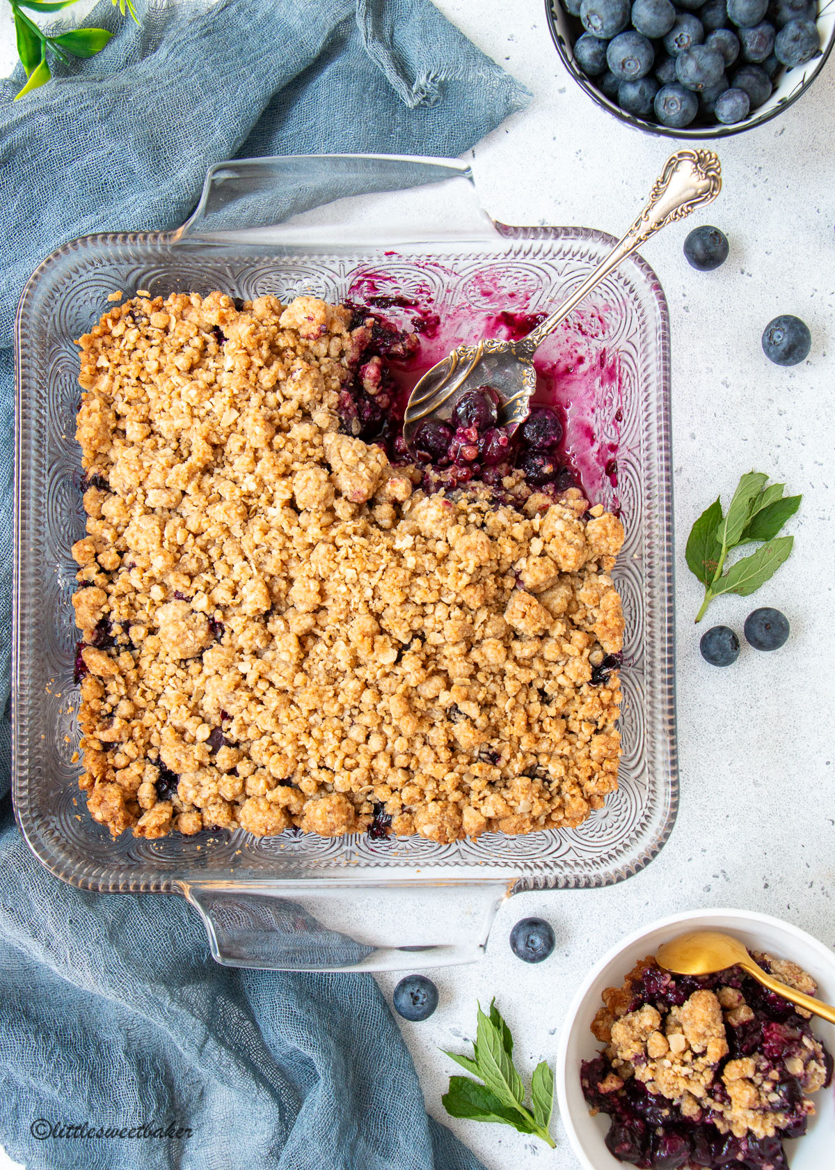 blueberry crisp in a baking dish with a serving spoon and some in a bowl.