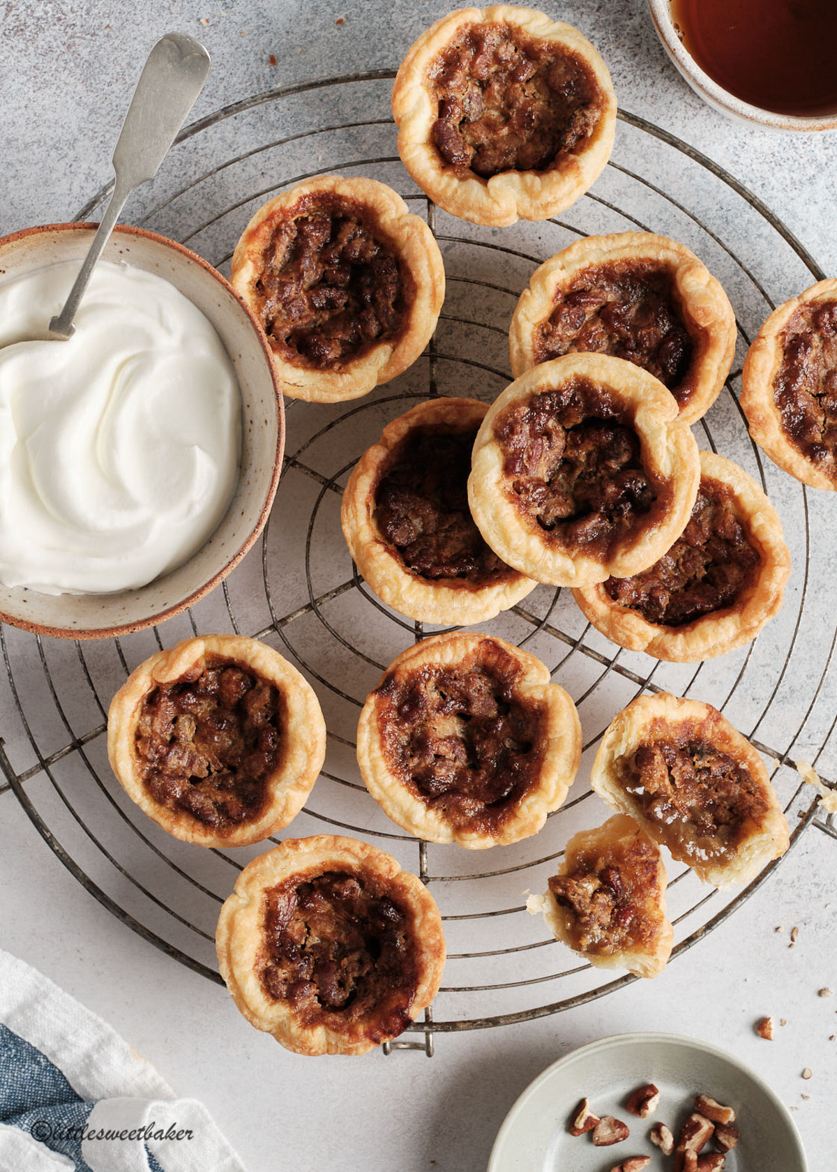 Butter tarts on a round cooling rack with a bowl of whipped cream.