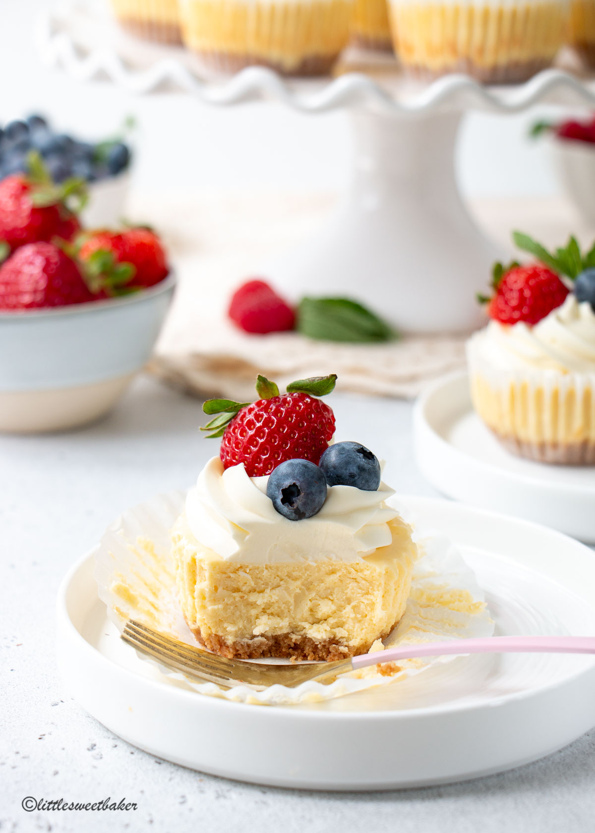 A mini cheesecake topped with whipped cream and berries on a white plate.