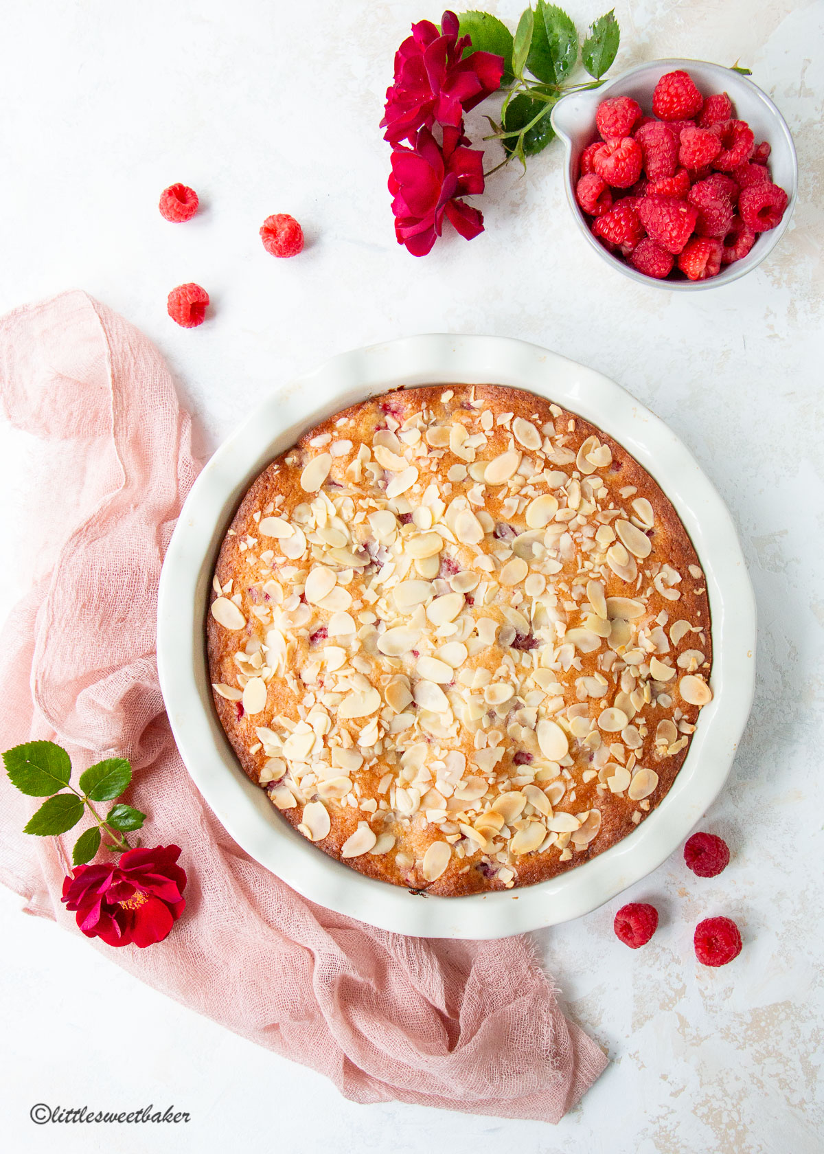 a raspberry almond cake surrounded by raspberries, red roses and a pink chiffon napkin
