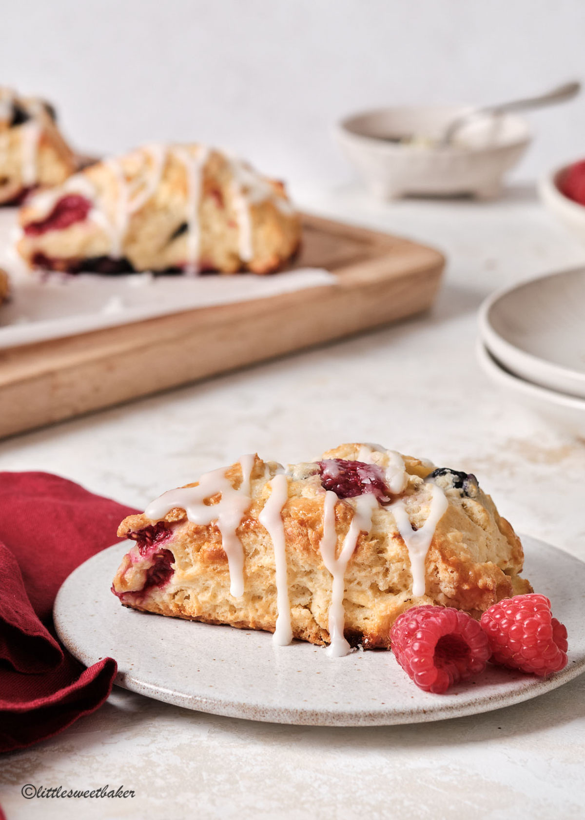 a beautiful glazed berry scone on a pottery plate with two fresh berries