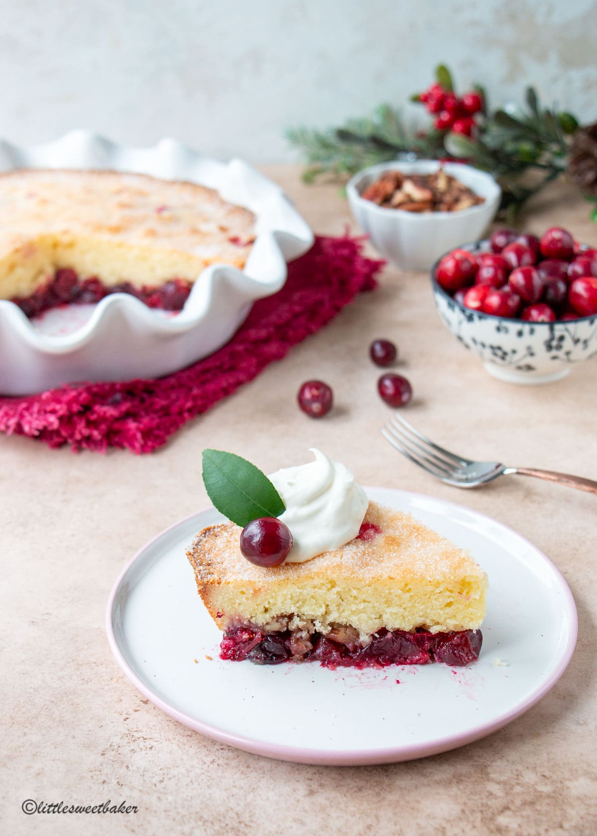 A slice of Nantucket cranberry pie topped with whipped cream, lemon leaf, and a fresh cranberry.