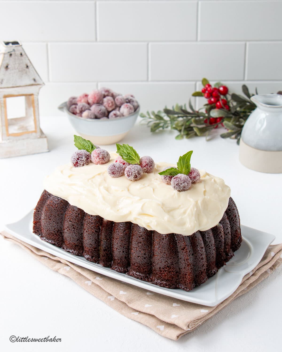 Gingerbread loaf topped with cream cheese frosting, sugared cranberries and mint leaves.