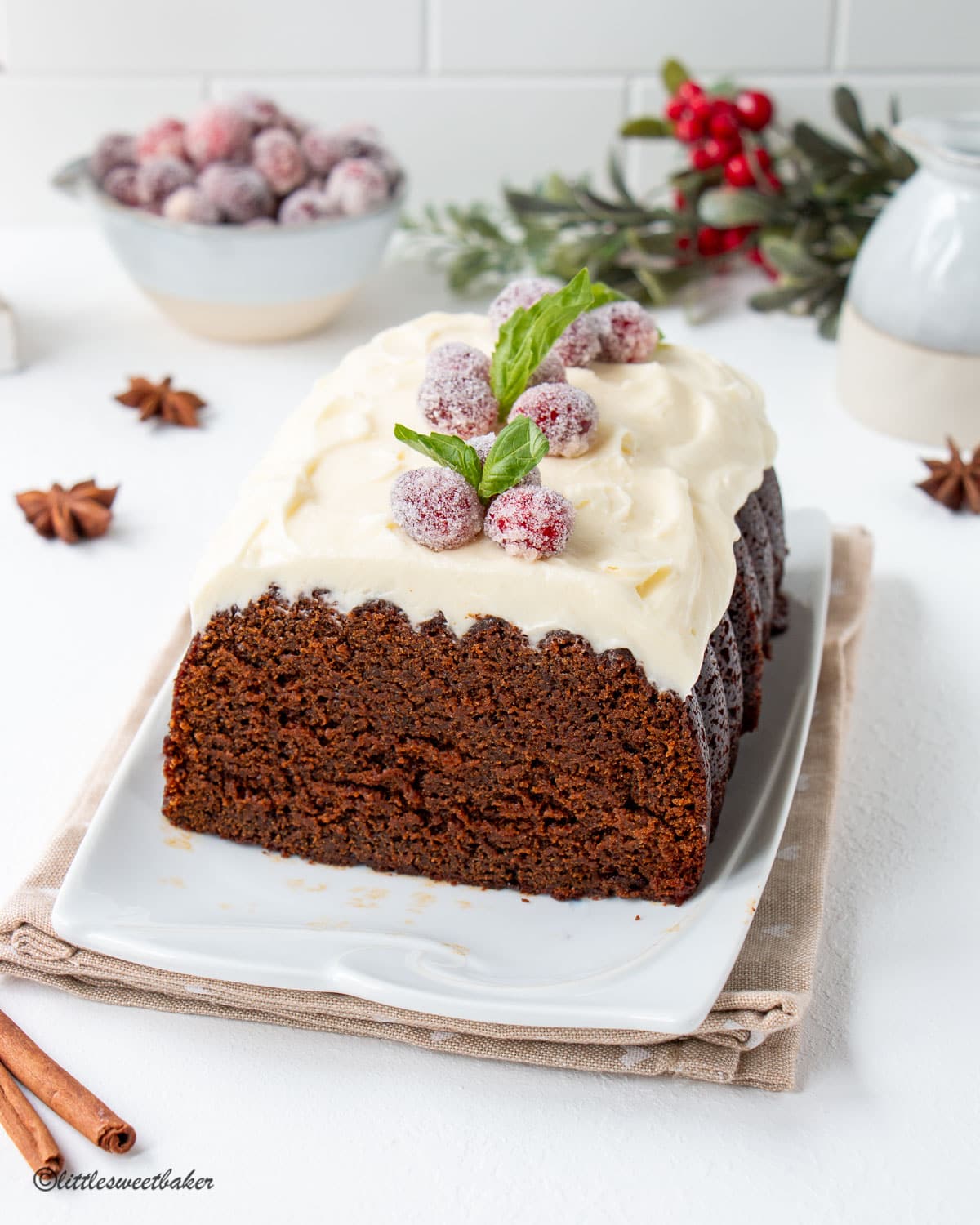 A cut gingerbread loaf with cream cheese frosting, sugared cranberries and mint leaves.