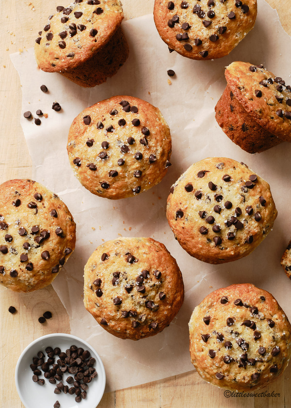 Overhead view of chocolate chip muffins on a wooden board and parchment paper.