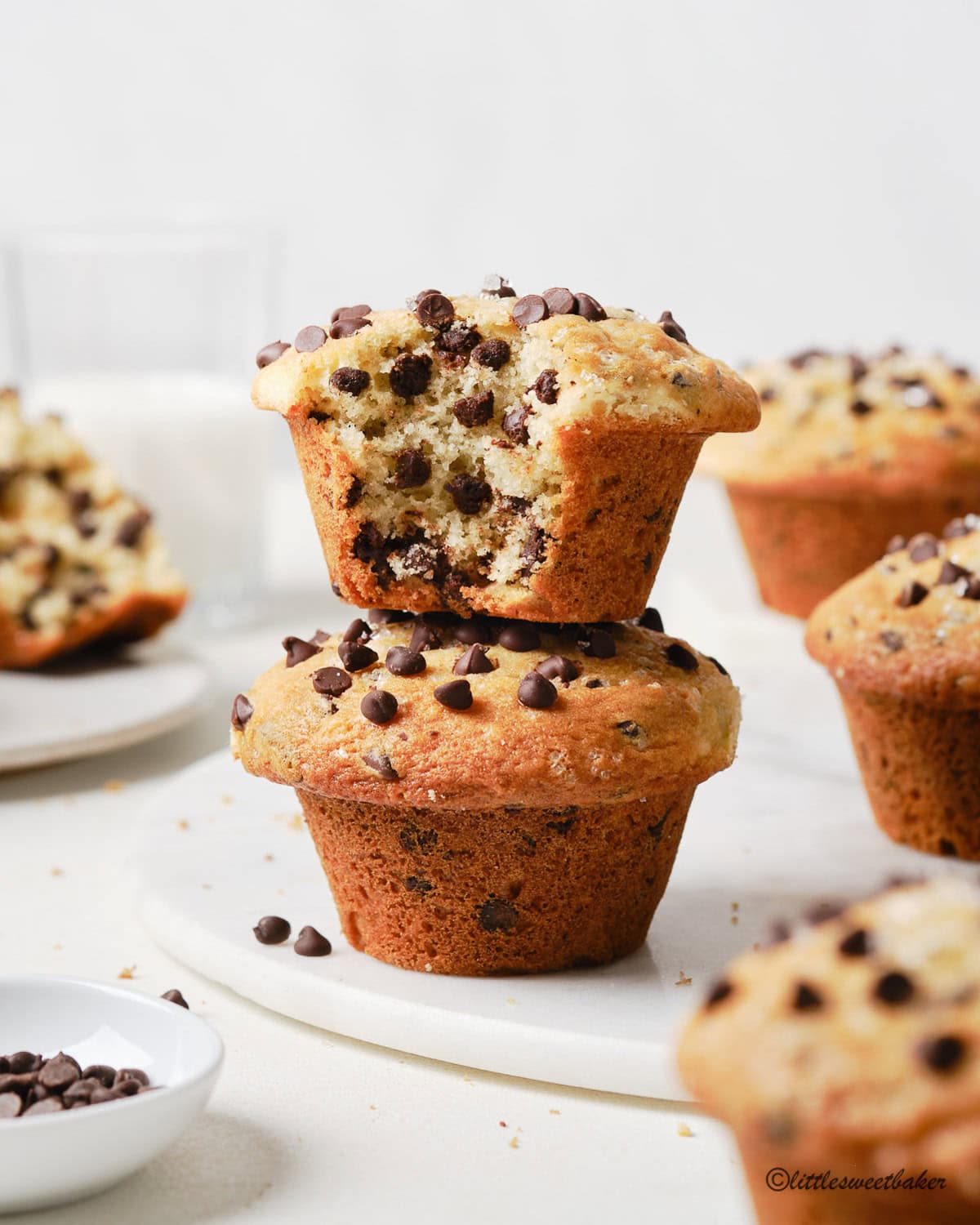 Two chocolate chip muffins stacked on a marble board with a bite taken out of the top one.