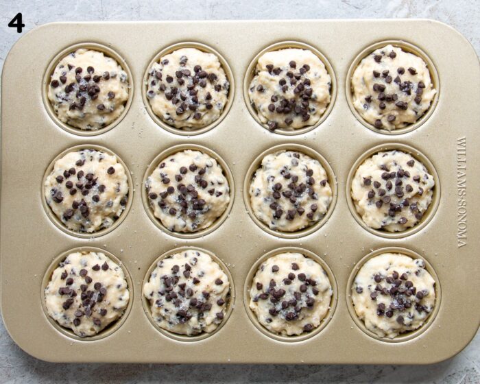 A gold muffin pan filled with chocolate chip muffin batter.