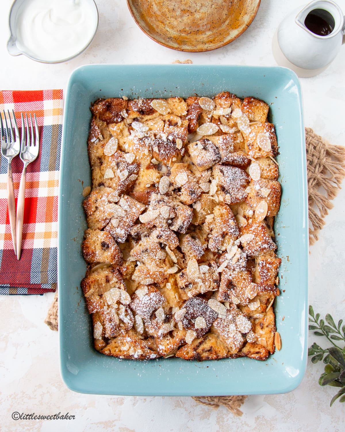 A whole casserole dish of panettone bread pudding topped with sliced almonds and powdered sugar.
