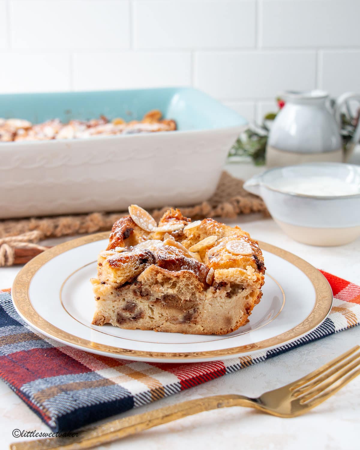 A slice of panettone bread oudding on a white and gold plate on a plaid napkin.