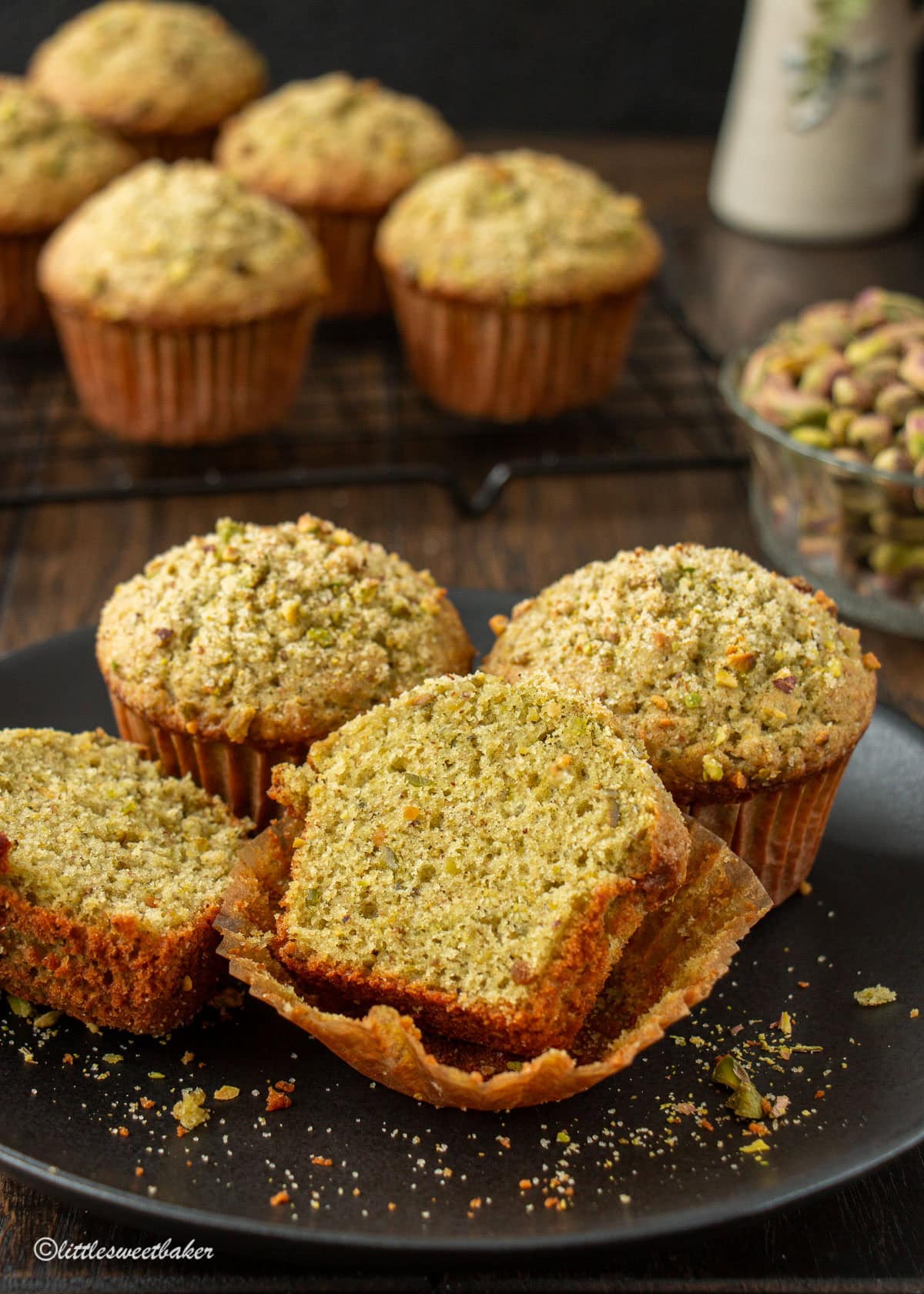 Three pistachio muffins in a black plate with one cut in half.