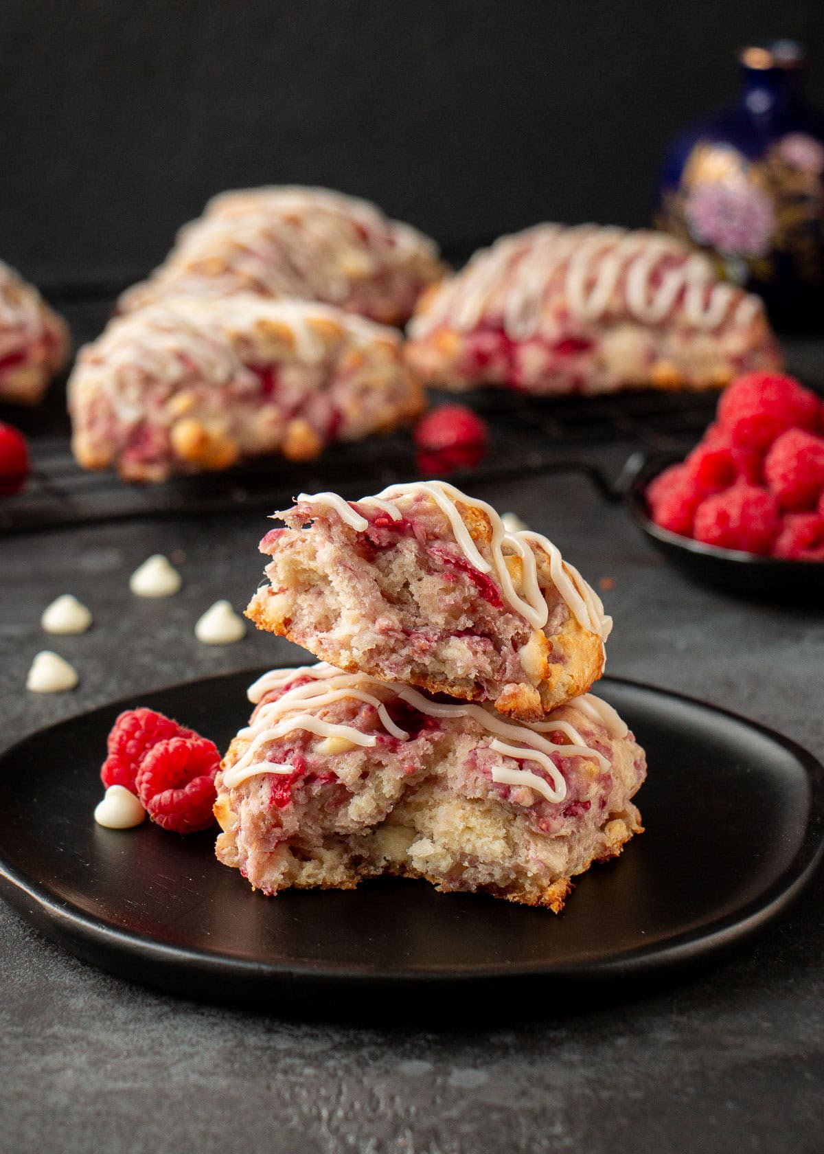 A raspberry scone with white chocolate chips broken in half on a black plate.
