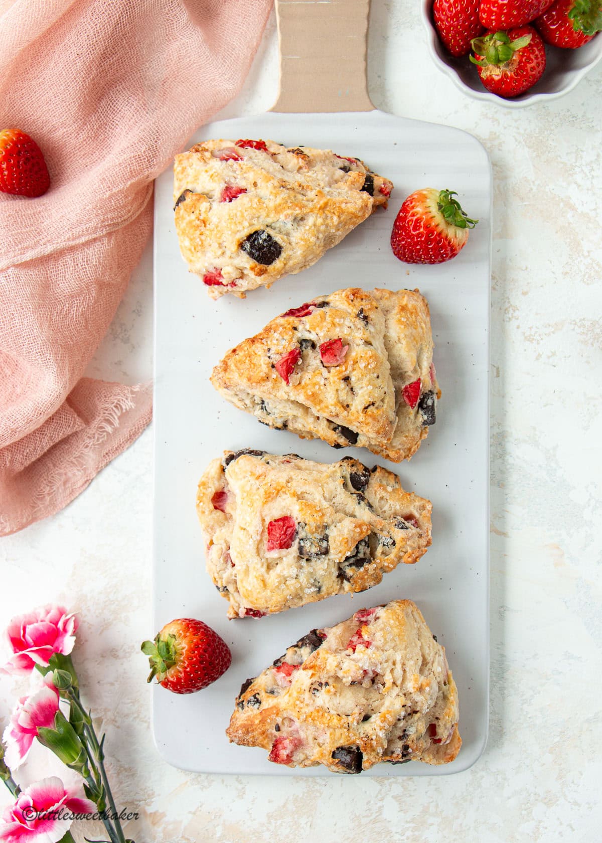 Four strawberry chocolate chunk scones on a white serving board.